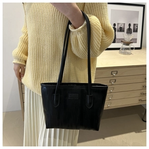 Detail of black PU leather tote bag featuring a square logo patch and fine vertical texture