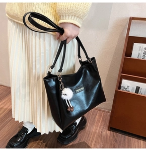 Detail of black patent leather tote bag with white plush charm and double shoulder straps
