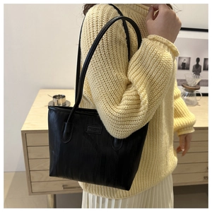 Detail of black tote bag with vertical texture and logo patch worn on a yellow sweater