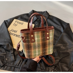 Detail of plaid wool tote bag with brown leather handles and rivets on black leather