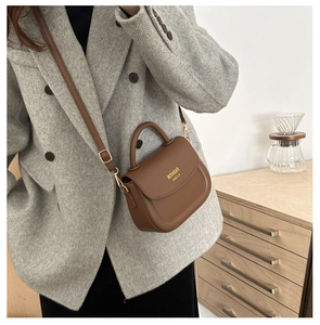 Close-up of a dark brown saddle bag with golden hardware and adjustable strap on a model