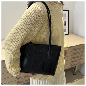 Close-up of black textured tote bag with rectangular leather label and slim shoulder straps