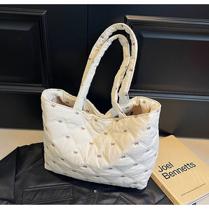 Detail of quilted tote bag featuring brown bow embroidery and a wide shoulder strap
