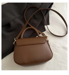 Top view of a dark brown leather saddle bag on white fabric with gold metal hardware
