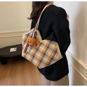 Detail of checkered tote bag featuring a V-shaped top and brown teddy bear charm accessory