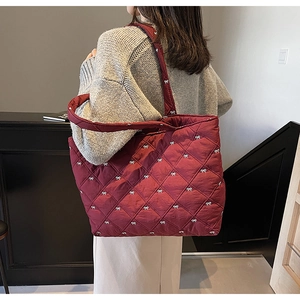 Deep red quilted tote bag with white bow prints shown on a woman's shoulder in casual style