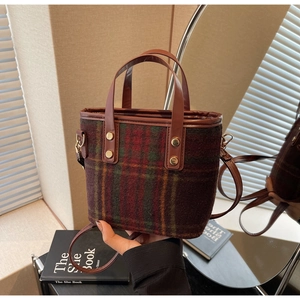 Detail of retro woolen tote bag with red and green plaid pattern and leather handles