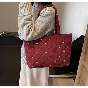 Detailed side view of a burgundy quilted tote bag featuring white bow embroidery pattern