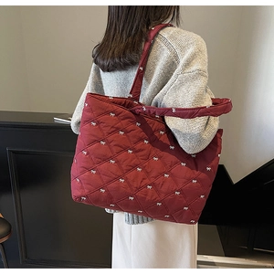 Detail of burgundy quilted tote bag with white bow embroidery and spacious interior