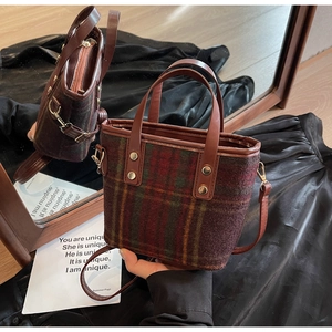 Detail of red and green plaid woolen bucket bag with brown leather handles and studs