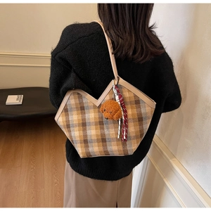 Detail of plaid tote bag featuring a V-shaped top, brown teddy charm, and striped silk scarf