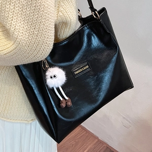 Black glossy leather tote bag with fluffy doll pendant shown from a side perspective