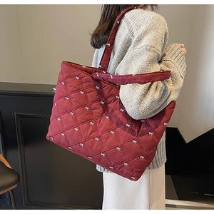 Detail of burgundy quilted tote bag with white bow embroidery and diamond pattern texture
