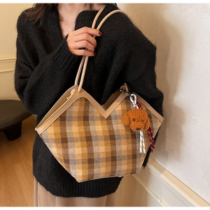 Detail of checkered tote bag with plush puppy charm and warm brown plaid texture