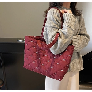Detail of burgundy quilted tote bag with white bow embroidery and spacious interior