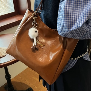 Brown leather tote bag with plush keychain shown in a vintage-style shoulder carry pose