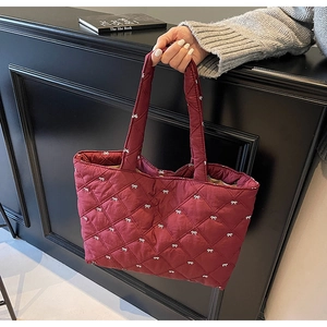 Detail of burgundy quilted tote bag with white bow patterns and soft padded texture