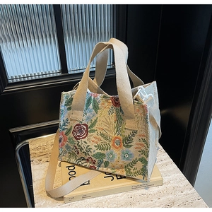 Detail of floral tapestry tote bag with beige canvas handles and side hook on marble surface