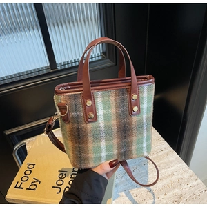 Detail of wool tote bag with green plaid texture, leather handle and gold rivet accents