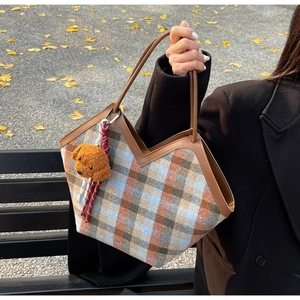 Detail of plaid tote bag with V-shaped cut and brown dog plush charm on outdoor bench