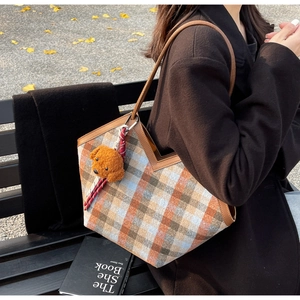 Close-up of retro plaid shoulder bag with brown leather trim and a cute plush bear charm