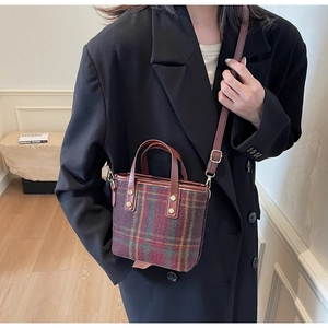 Close-up of retro plaid woolen tote with brown leather handles and gold metal rivets