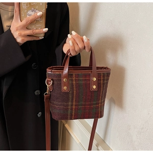 Detail of red and brown plaid wool bucket bag with leather handles and gold metal rivets