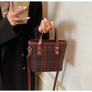 Detail of wool plaid bucket bag featuring leather handles and gold rivet accents