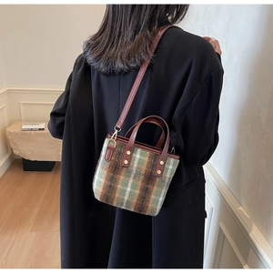 Detail of green plaid wool tote bag with brown leather handles and golden rivets