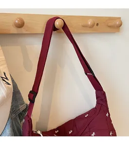 Detail of burgundy quilted bag with white bow embroidery and adjustable shoulder strap
