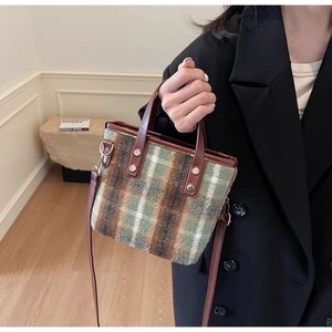 Close-up of plaid wool bucket bag with brown leather handles and gold rivet details