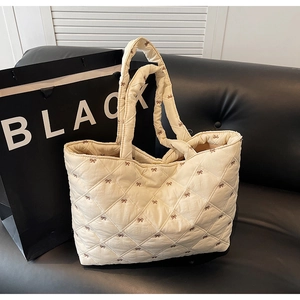 Detail of cream quilted tote bag with brown bow embroidery and soft fabric texture