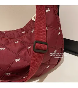 Detail of adjustable shoulder strap and bow pattern on burgundy quilted crossbody bag