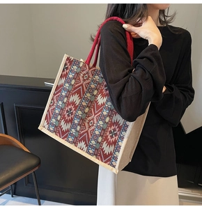 Detail view of woven tribal pattern tote bag with red rope handle on a female model