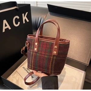 Detail of red and green plaid woolen bucket bag with brown leather trim and gold studs