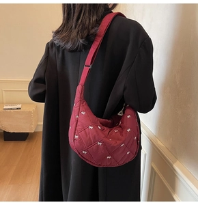Detail of burgundy quilted crescent bag with bow embroidery and wide adjustable strap