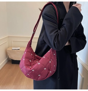 Detail of burgundy quilted crescent bag with white embroidered bows and shoulder strap