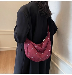 Quilted deep red crescent bag with white bow patterns worn as a crossbody shoulder bag