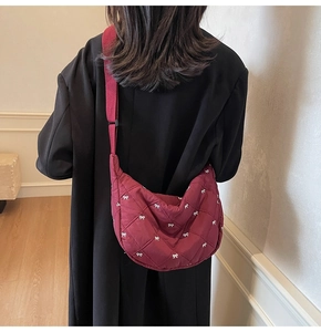 Quilted burgundy crescent bag with white bow pattern shown on a shoulder