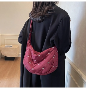 Close-up of wine red quilted half-moon bag featuring white bow embroidery and wide strap