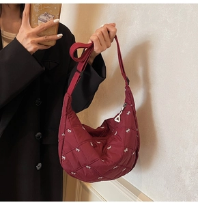 Detail of burgundy quilted crescent bag with small white bows and adjustable strap