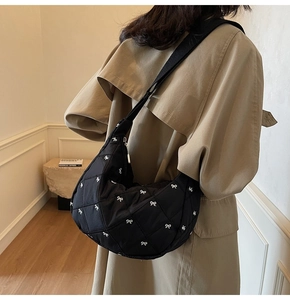 Detail of a black quilted shoulder bag with bow embroidery shown on a model