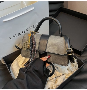 Détail du sac bandoulière en denim gris et cuir noir avec pendentifs dans un coffret