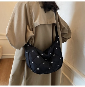 Close-up of black quilted shoulder bag with white bow patterns on khaki trench coat