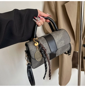 Détail d'un sac à main en daim gris et cuir noir avec breloque raquette et corde tressée