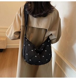Detail of black quilted crossbody bag with white bow embroidery and wide shoulder strap