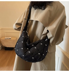 Close-up of black quilted crescent bag with bow embroidery worn with a beige coat
