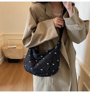 Close-up of black quilted nylon crossbody bag with white bow embroidery on trench coat
