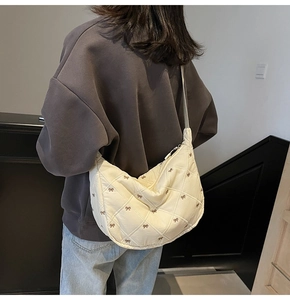 Quilted off-white crescent crossbody bag with bow patterns worn by a model from behind