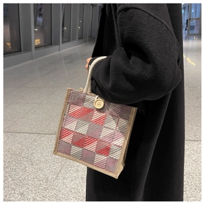 Detail of red and grey checkered woven tote bag with button closure on black coat